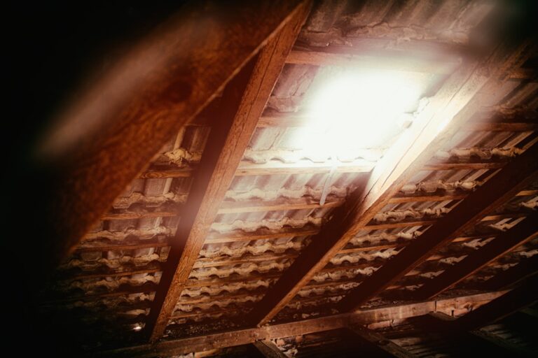 Insulation being installed across an attic floor around roof framing and ventilation baffles.