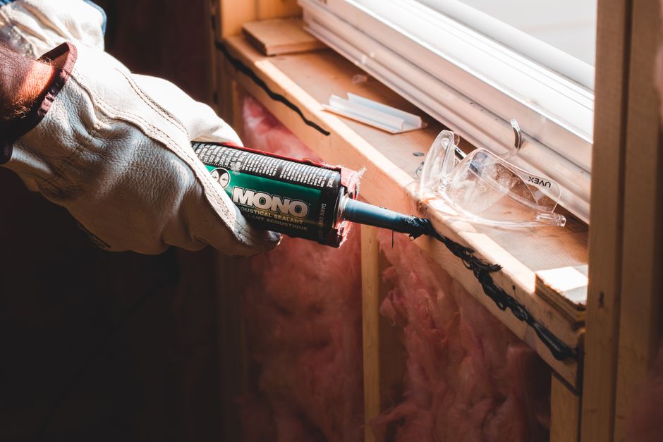 Homeowner examining attic insulation beside roof framing and sealed wiring penetrations